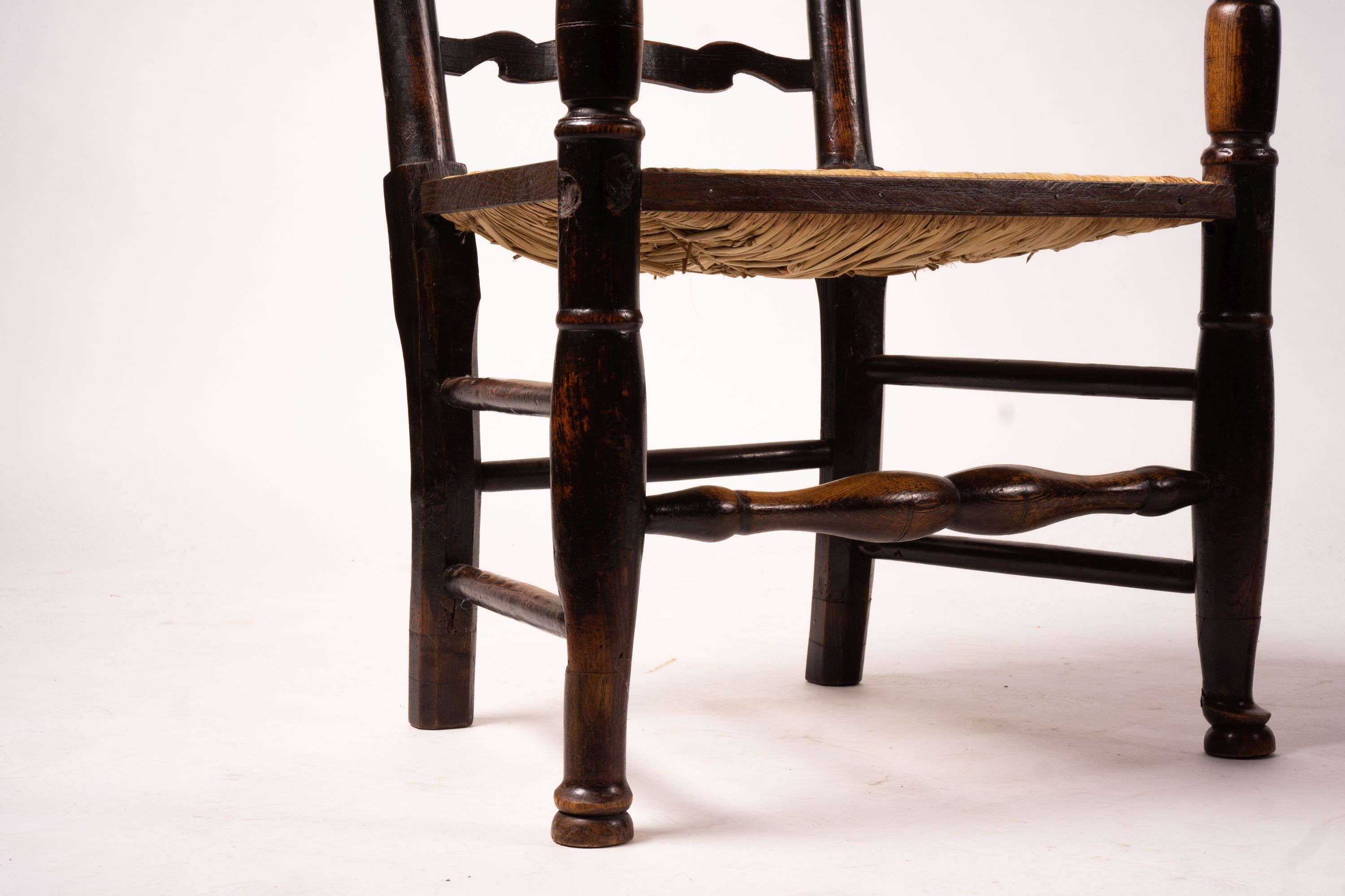 A pair of early 19th century Lancashire ash and fruitwood rush seat ladderback elbow chairs, width 60cm, depth 46cm, height 110cm